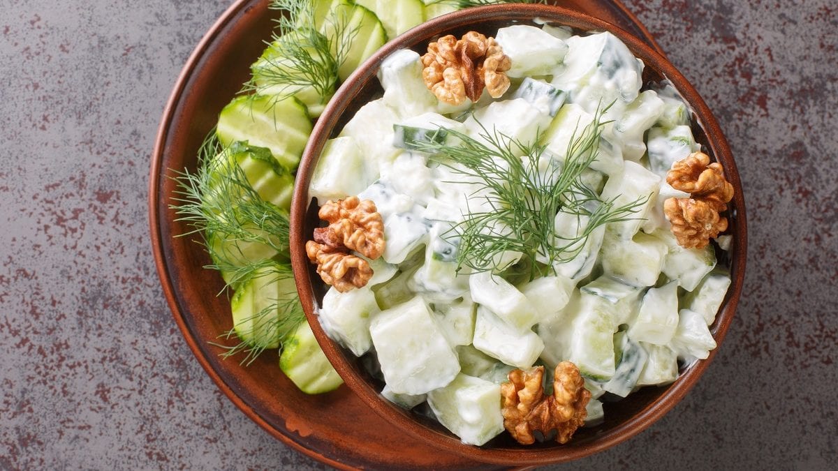 eine Schüssel mit Snezhanka steht auf einem tisch. es handelt sich um einen Gurkensalat mit Joghurt.