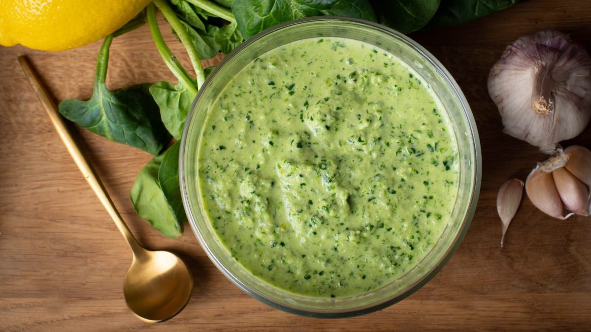 Ein Gefäß mit Spinat-Knoblauch-Sauce neben einem Kupferlöffel.