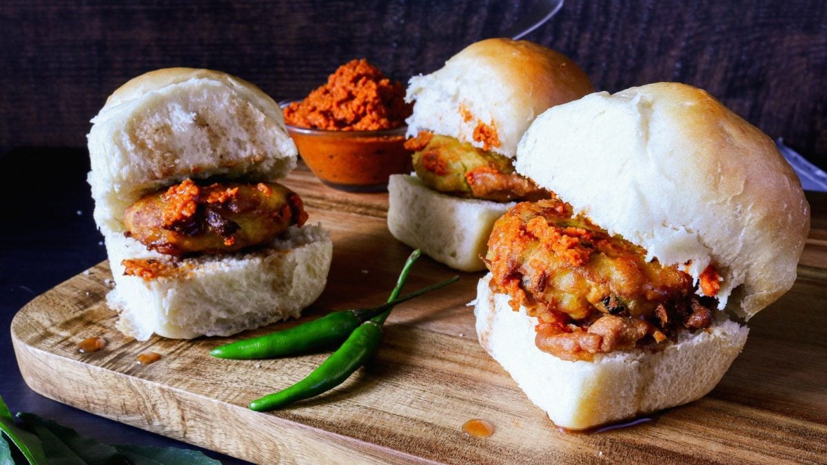 Vada Pav indischer Street Food Burger aus Kartoffeln, vegan, mit grünen Chilis, Paste in einer Schale auf Holzbrett. Frontalansicht.