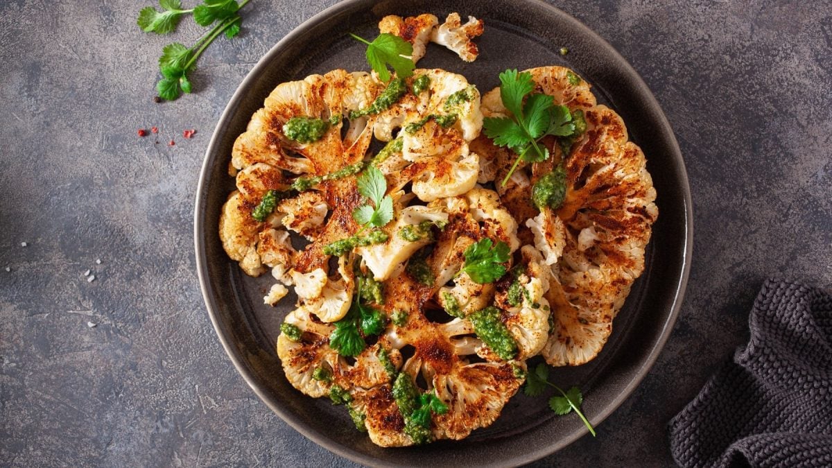 Ein Teller mit veganen Blumenkohlschnitzeln und frischen Kräutern in der Draufsicht.
