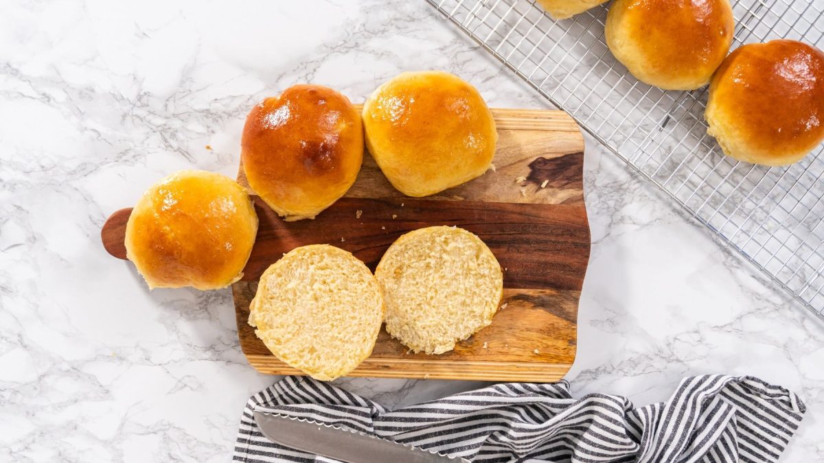 vegane Brioche-Brötchen auf einem Holzbrett und einem Gitter in der Draufsicht, eins davon ist aufgeschnitten.
