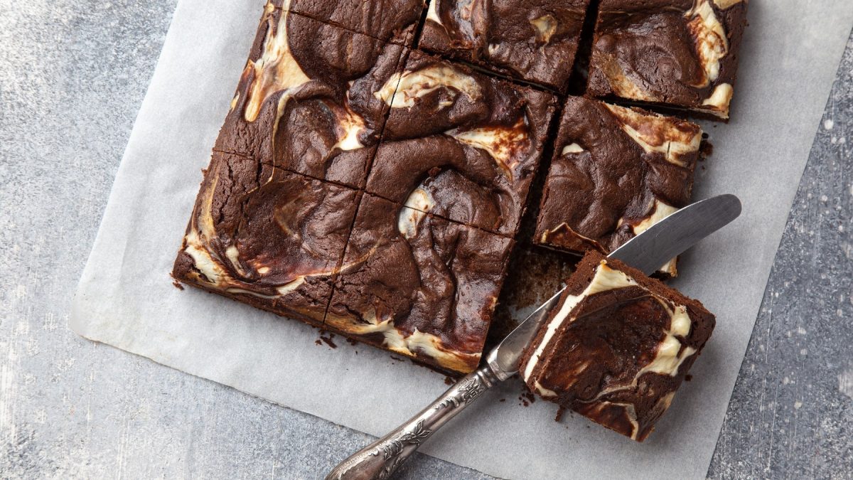 vegane Cheesecake Brownies auf einem Stück Backpapier in der Draufsicht, daneben ein Messer.