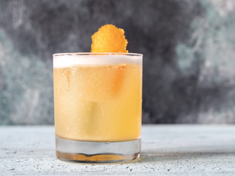 Ein Glas veganer Whiskey Sour mit einer Orangenzeste.