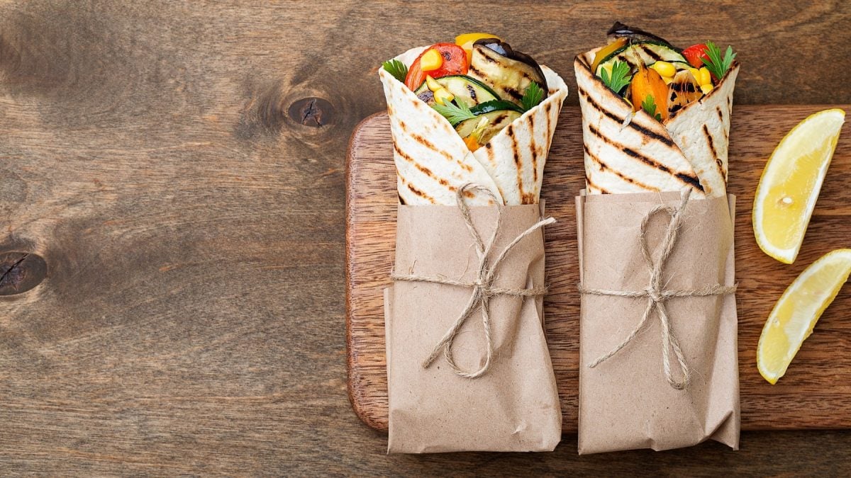 Zwei Wraps vom Grill, eingepackt in Packpapier, daneben Zitronenspalten. Alles Draufsicht.