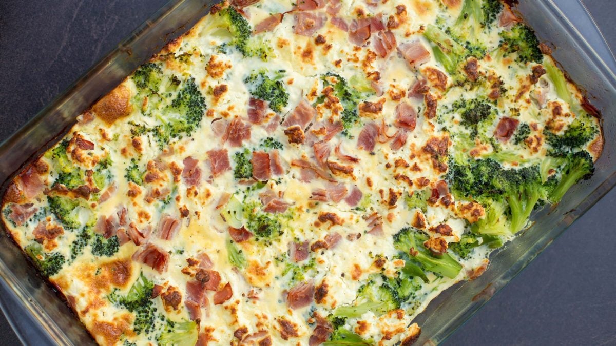 Brokkoli-Gratin mit Schinken in gläserner Form auf grau-blauem Untergrund.
