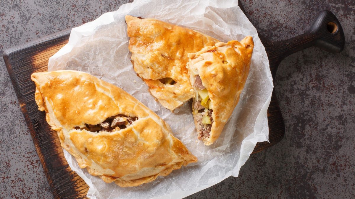 Ein dunkles Holztablett mit Cornish Pasty darauf.