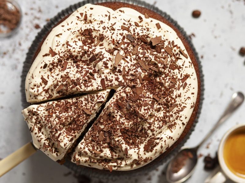 Irish-Coffee-Kuchen mit Schlagsahne und geriebener Schokolade in einer Form. Daneben steht eine Tasse Kaffee.