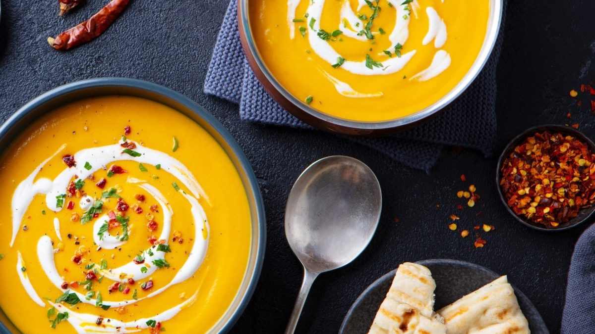 Zwei Teller voll Kürbissuppe mit Erdnussbutter und Kokosmilch auf dunklem Untergrund.