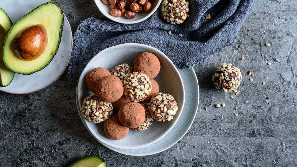 Eine hellblaue Schüssel mit Avocado-Schokoladen-Trüffeln neben frischer Avocado.