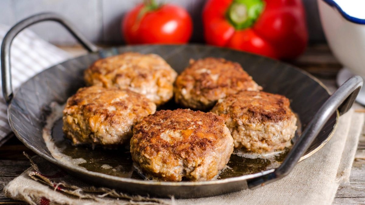 Draufsicht auf eine Pfanne mit 5 bayerischen Fleischpflanzerl. Im Hintergund liegen 2 rote Paprika.