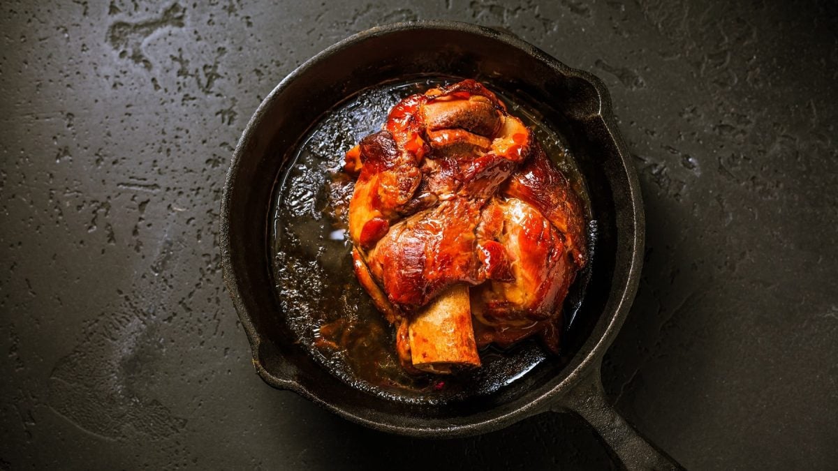 Eine bayerische Schweinshaxe in einer gusseisernen Pfanne in der Draufsicht.