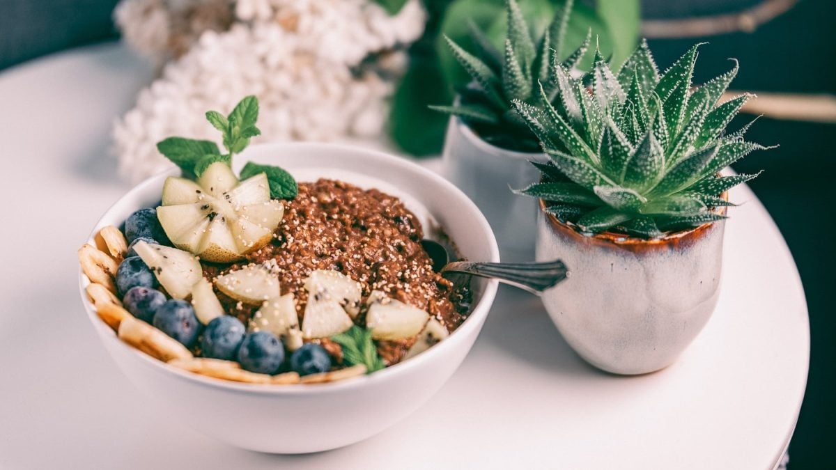 Eine Schüssel Buchweizen-Porridge mit Kakao und frischem Obst, daneben kleine Sukkulenten.