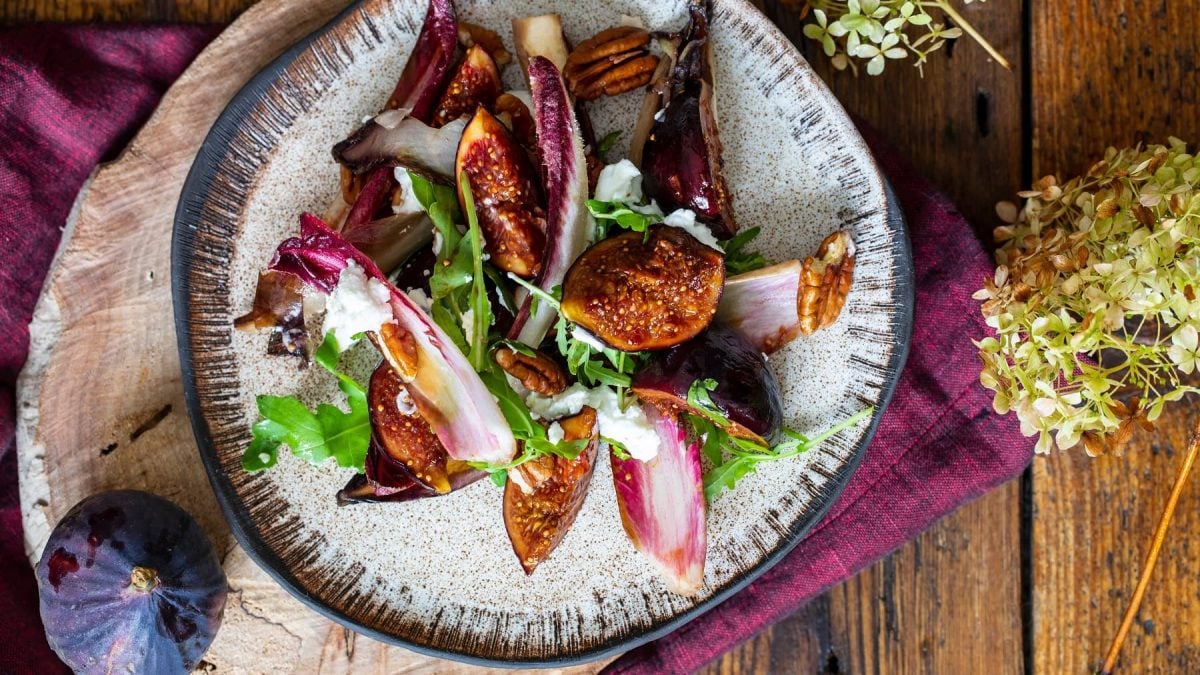 Chicoréesalat mit karamellisierten Feigen und Rucola sowie Feta auf einem Teller in der Draufsicht.