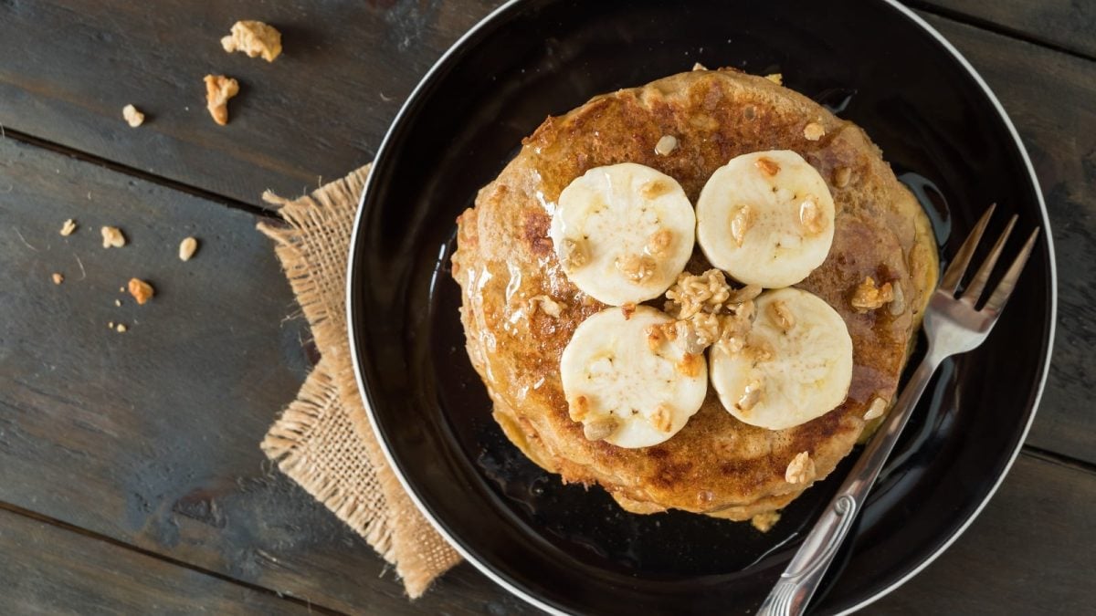 Ein schwarzer Teller mit Bananen-Pancakes auf einem braunen Tuch.