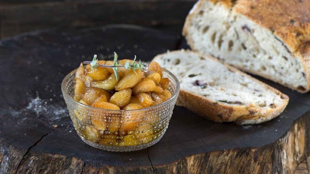 Ein Glas mit Knoblauch-Konfit neben Brot auf einer Baumscheibe