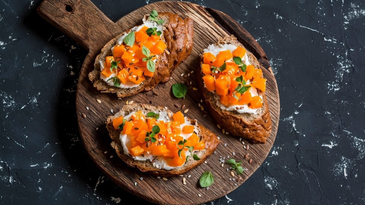 Ein Holzbrett mit Kürbis-Bruschetta mit Ziegenkäse darauf.