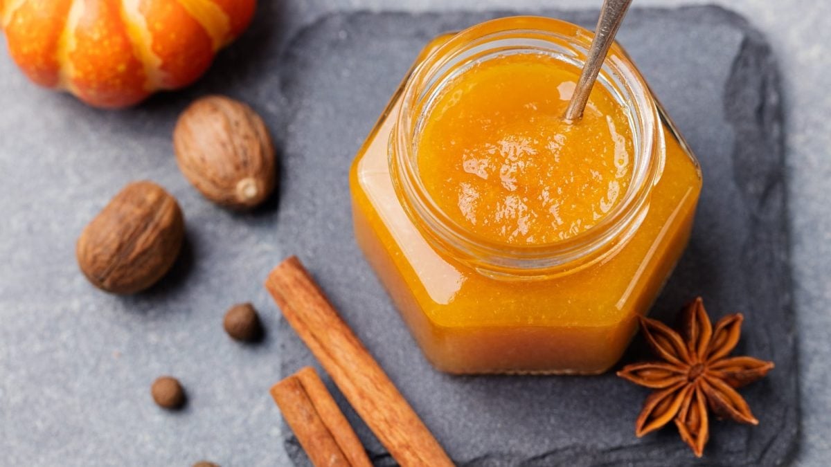 Ein Glas mit Kürbis-Marmelade, das auf einer Schieferplatte steht neben Gewürzen.