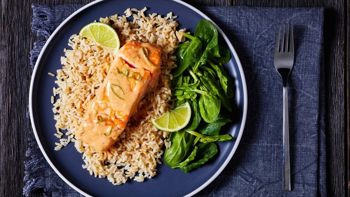 Ein dunkler Teller gefüllt mit Lachs in Kokos-Limetten-Sauce.