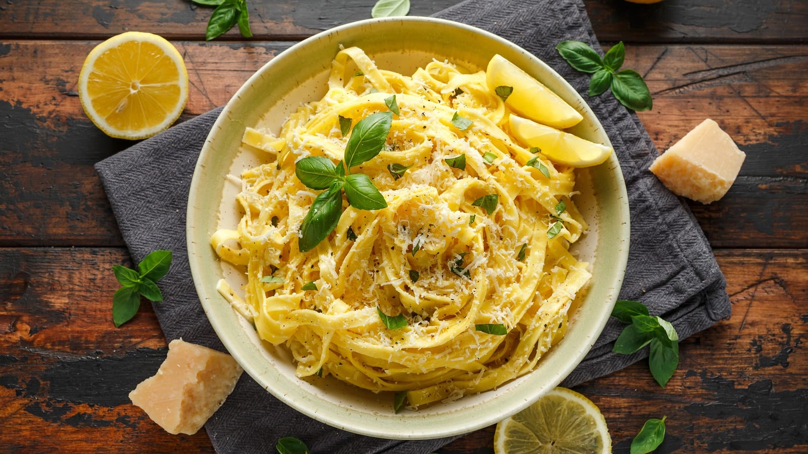 Ein runder weißer Teller mit Pasta mit Schmelzkäse neben Zitronenscheiben und Käseblocken.