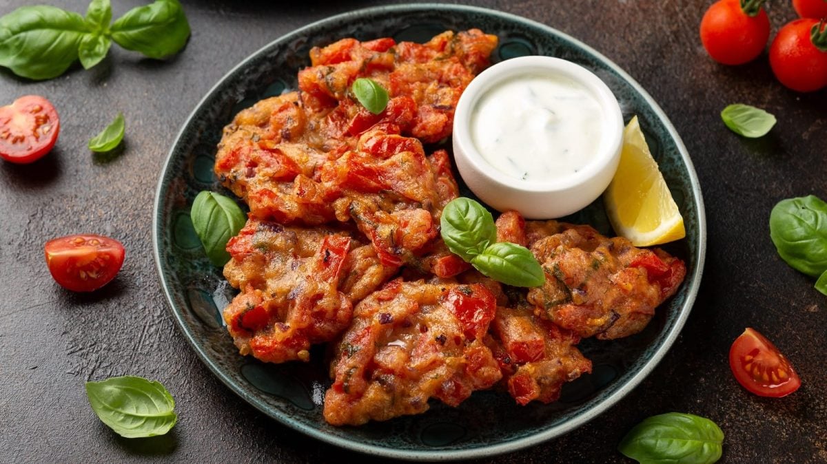 Ein schwarzer Teller mit Tomatokeftedes und einem Dip.