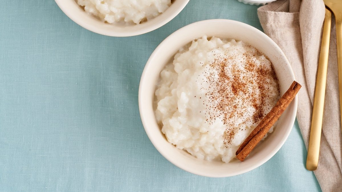 Eine Schüssel mit veganem Milchreis mit Zimtstange auf hellblauem Hintergrund
