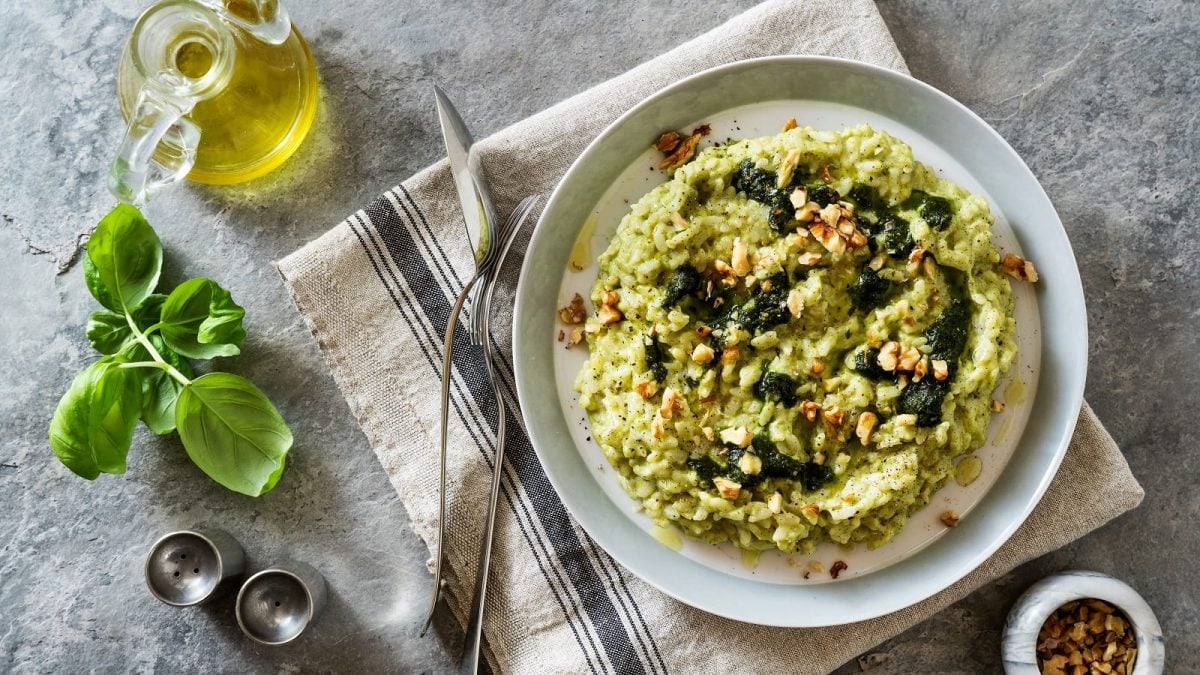 EIn Teller mit Zucchini-Risotto mit Pesto auf einem grauen Geschirrtuch neben frischen Zutaten.