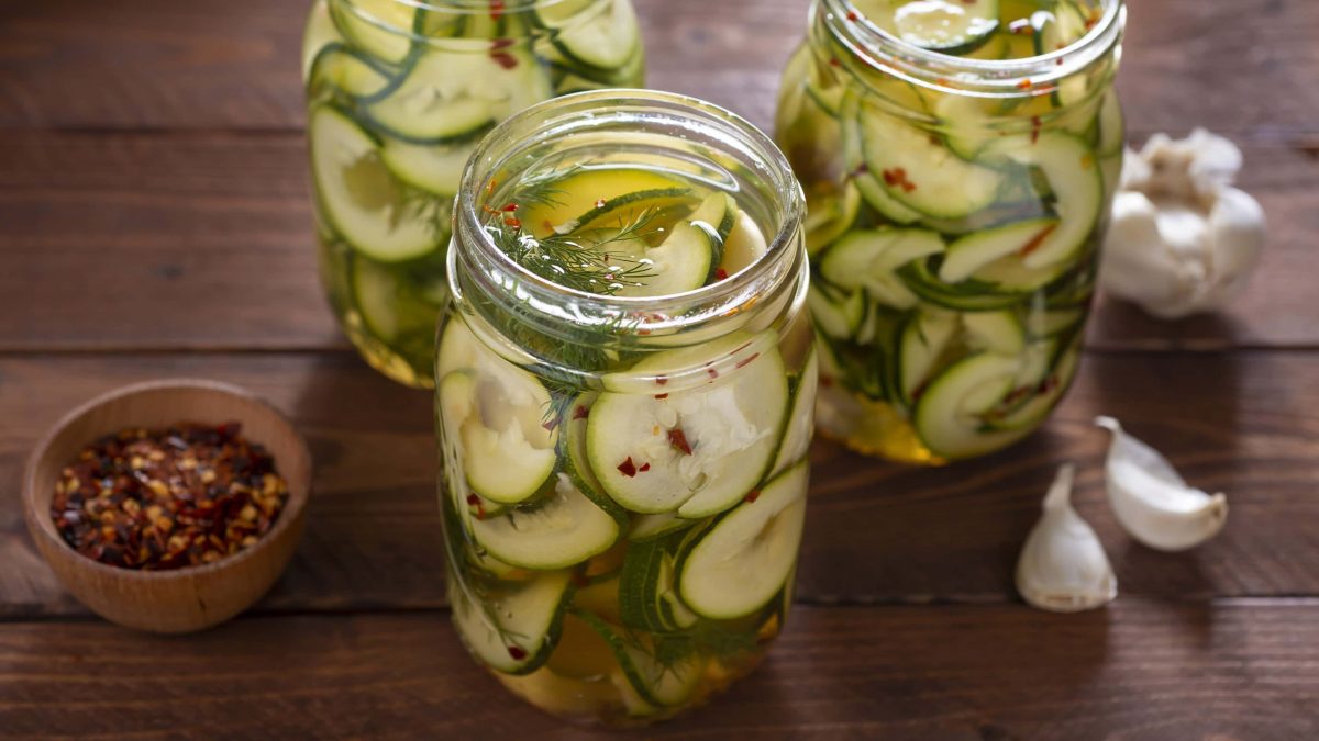 Eingelegte Zucchini7, in Scheiben geschnitten eingemacht in einer Mischung aus Essig, Kräutern und Chili, geöffnet serviert auf einem Holzbrett.