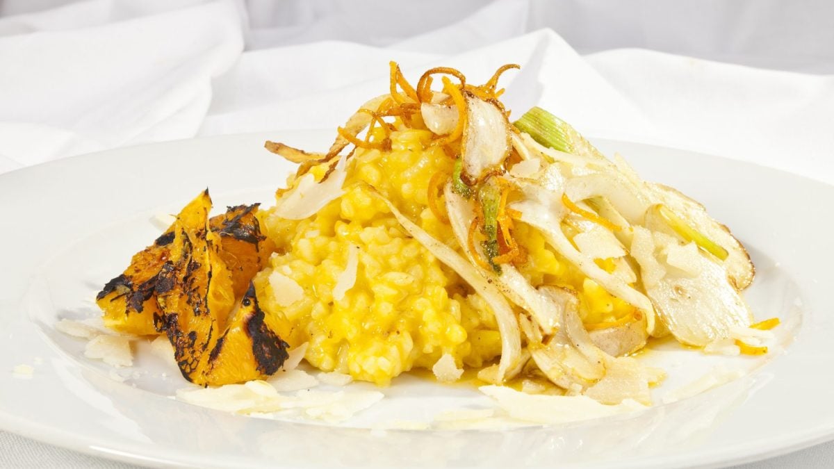 Fenchel-Risotto mit Safran und geflämmten Orangen auf weißem Teller vor hellem Hintergrund. Frontalansicht.