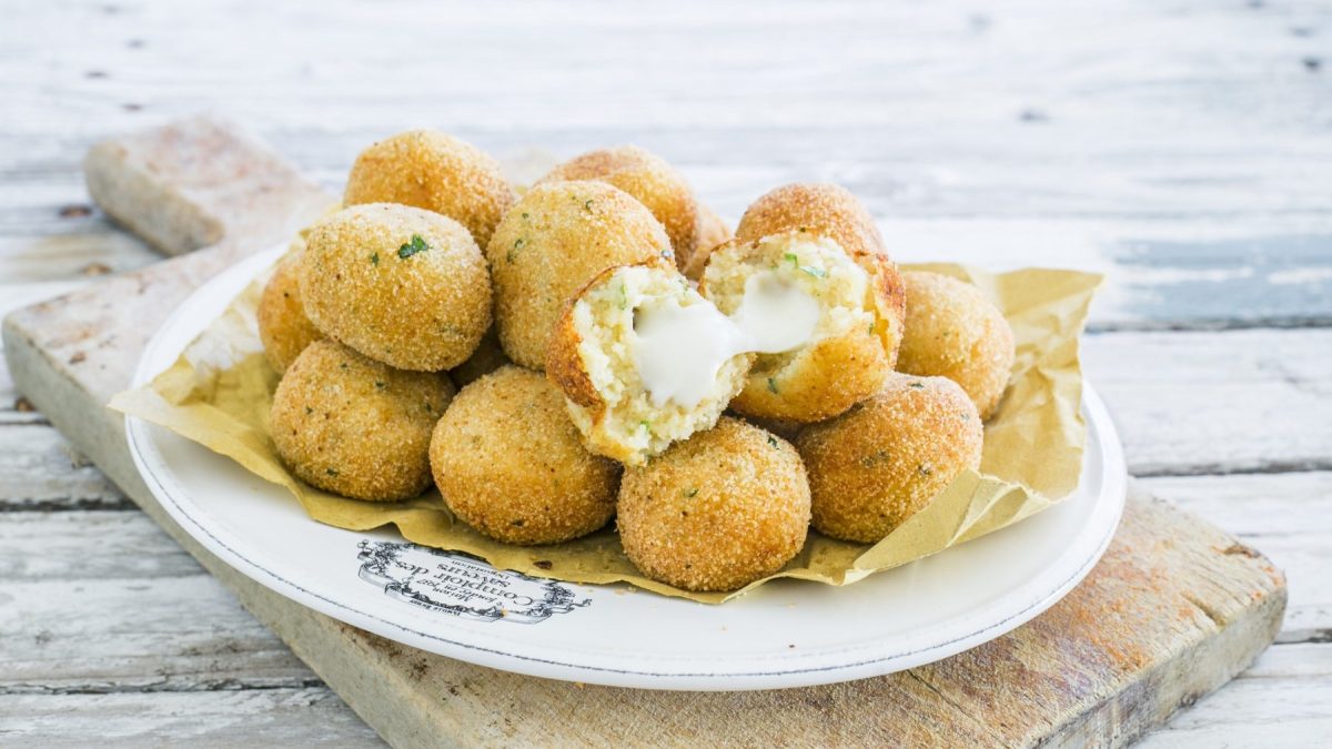 Frittierte Kartoffelbällchen mit Käsefüllung auf einem weißen Teller. Der Teller steht auf einem Holzbrett.