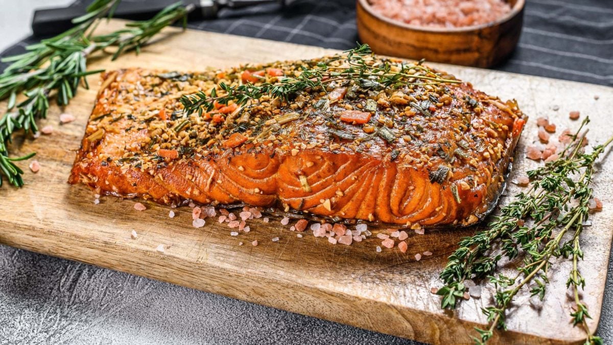 Gewürzlachs vom Grill auf Holzbrett mit Kräutern. Daneben rosa Salz. Draufsicht.