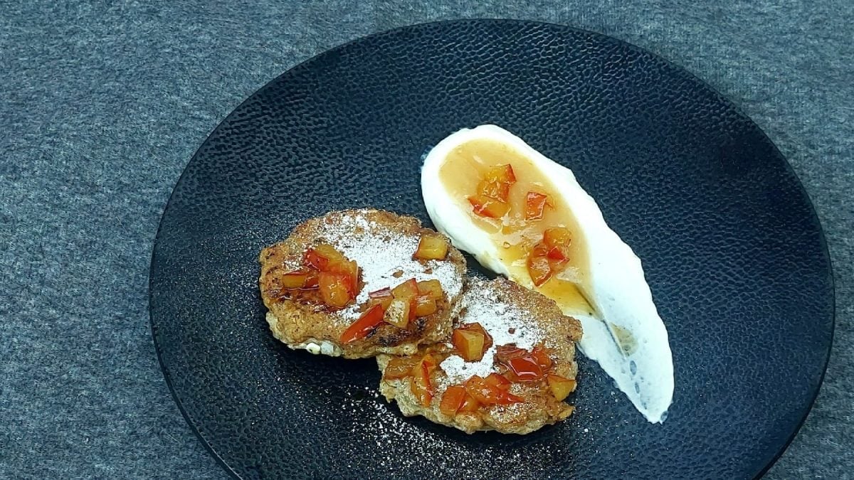 Ein schwarzer Teller mit zwei Hafer-Pancakes, Skyr , Apflemus und Apfelstückchen auf einem matt-grauen Untergrund.