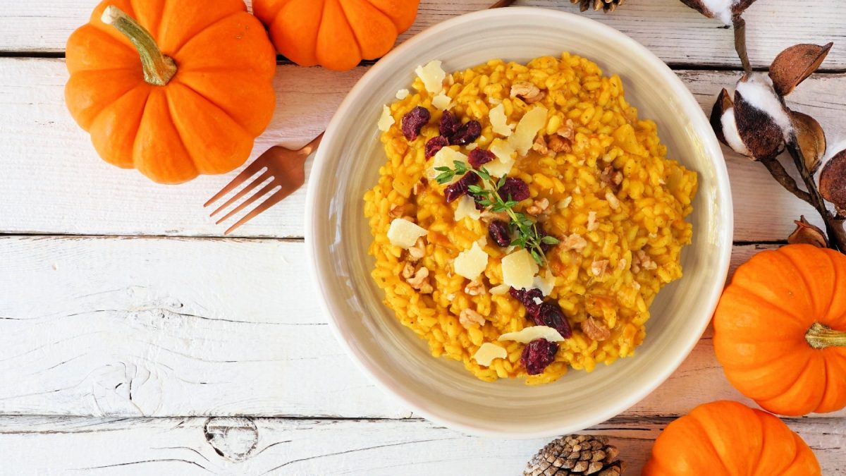 Ein weißer Teller mit dem Herbst-Risotto auf einem weißen Tisch mit allerhand herbstlicher Dekoration.