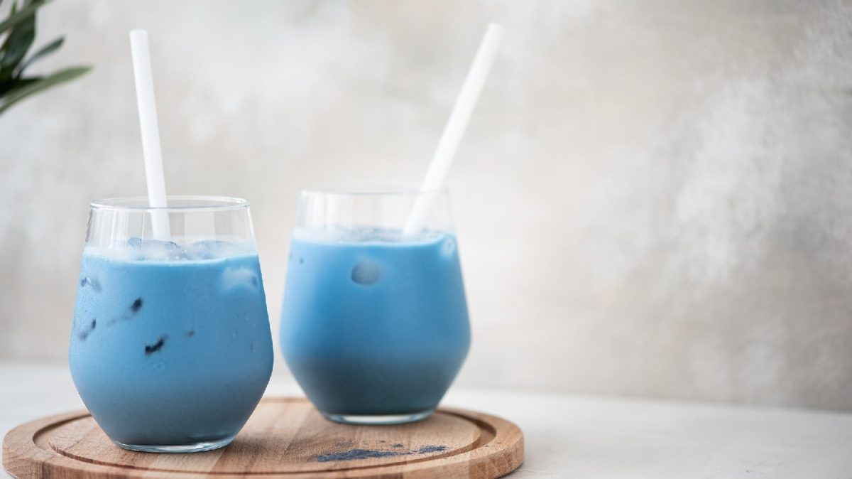 Zwei Gläser mit dem Kokosnuss-Latte und Spirulina auf einem kleinen Holzbrett mit zwei weißen Strohhalme.