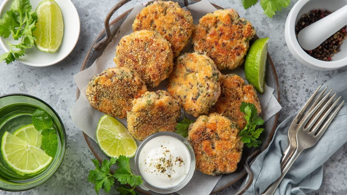 Ein Teller mit Lachs-Quinoa-Patties, frischen Limetten und einem Dip.