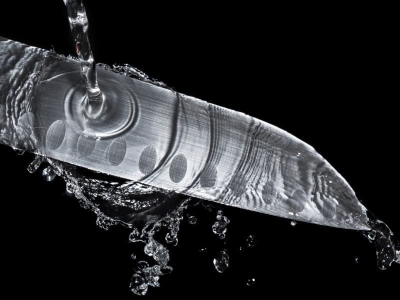 Ein Messer unter einem laufenden Wasserhahn und schwarzem Hintergrund.