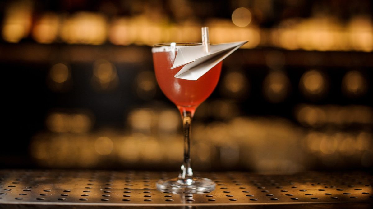 Paper Plane mit Papierflieger auf Thresen. Im Hintergrund unscharf eine Bar. Frontalansicht.