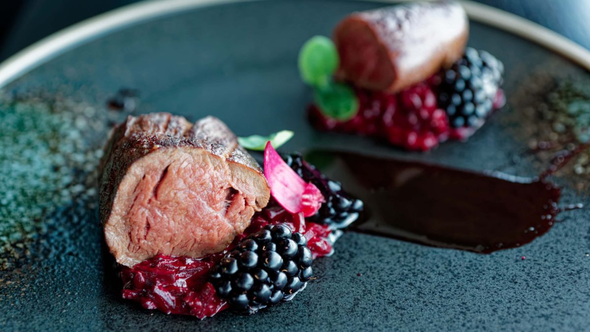 Angeschnittener Rehrücken auf einem blauen Teller mit dem roten Rübenrelish und dunkler Sauce.