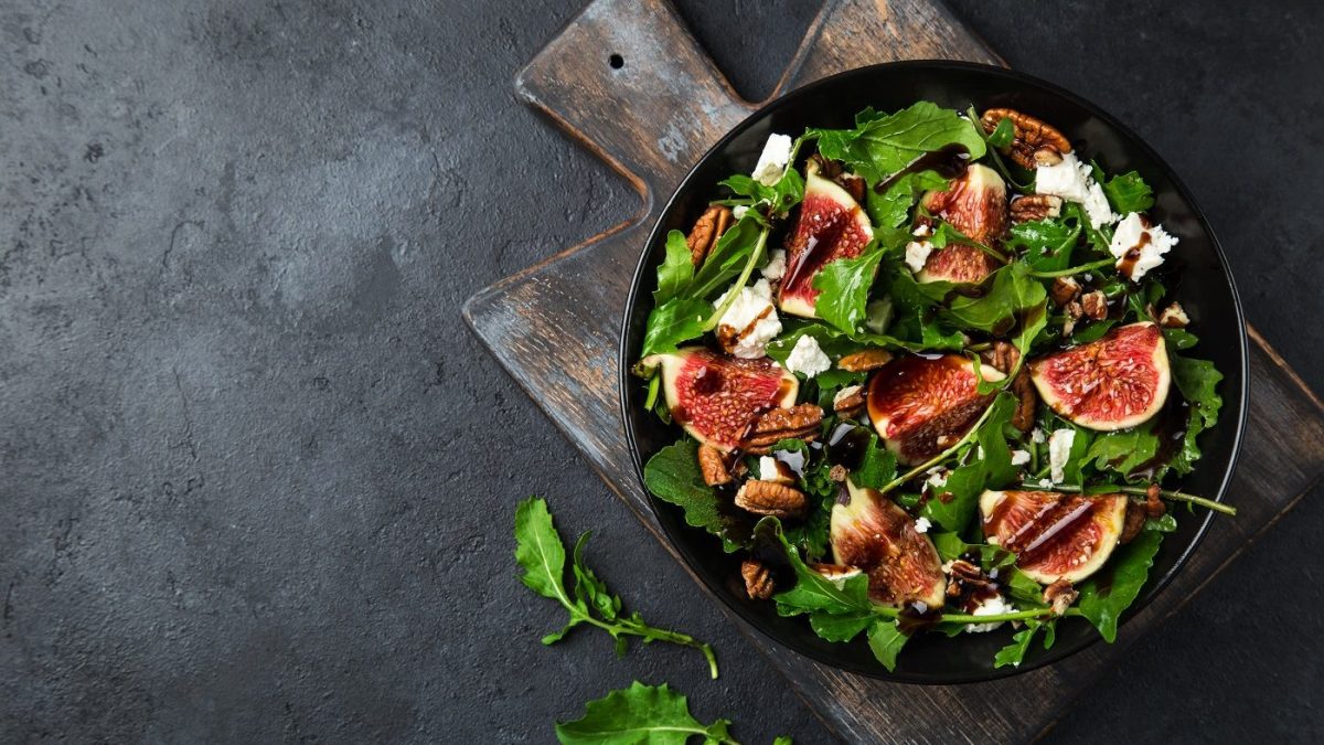 Aus der Vogelperspektive: Ein Rucola-Salat mit Feigen, Nüssen und Feta auf einem dunklen Untergrund