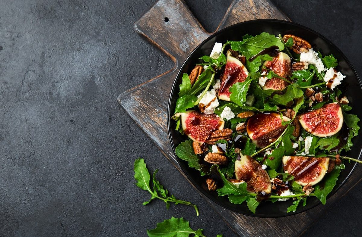 Aus der Vogelperspektive: Ein Rucola-Salat mit Feigen, Nüssen und Feta auf einem dunklen Untergrund