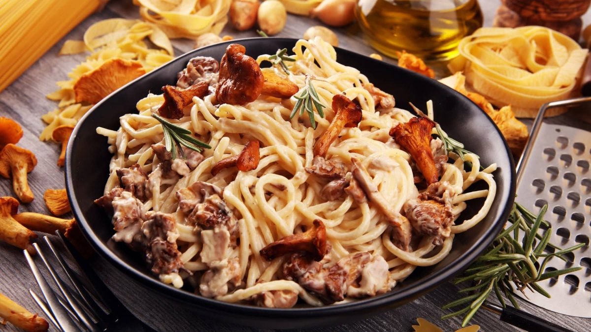 Ein Teller Spagehtti mit veganer Pfifferling-Rahmsauce, drumherum liegen die Zutaten verstreut.