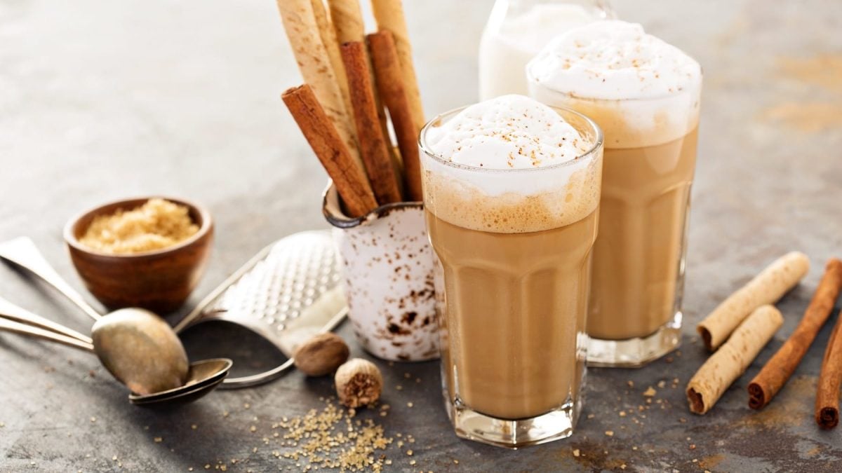 Zwei Gläser Spiced Latte mit Milchschaum, drumherum Gewürze wie Zimtstangen und Muskatnüsse.
