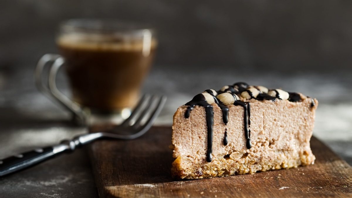 Ein Stück veganer Schoko-Cheesecake, daneben eine Gabel und eine Tasse Kaffee.