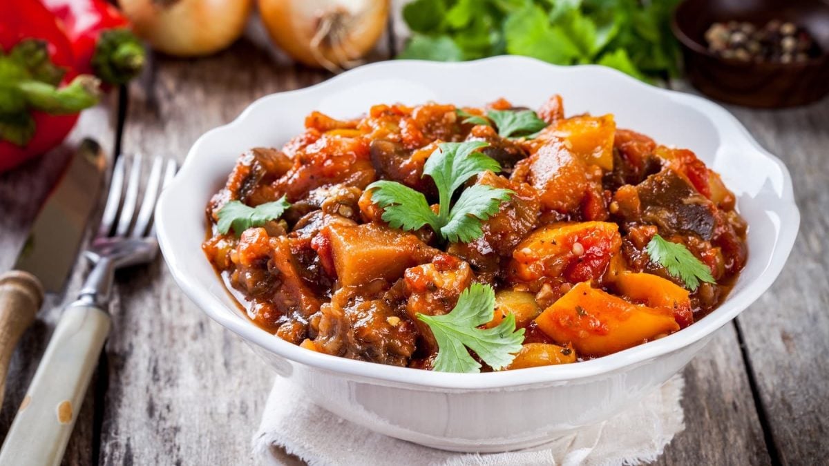 Ein tiefer Teller veganes Gemüsegulasch mit Petersilie bestreut, daneben liegen Gabel und Messer