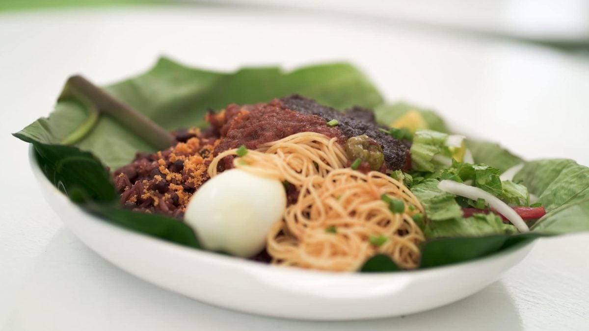 Waakye Streetfood aus Ghana mit Ghana Shito, Lammgulasch, Ei und Nudeln auf Bananenblatt auf weißem Teller. Frontalansicht.