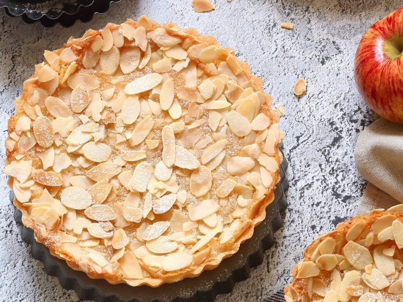 Apfel-Schüttelkuchen mit Mandeln auf grauer Oberfläche.