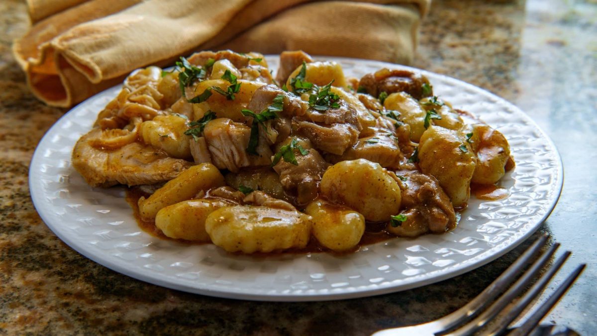 Gnocchi-Gulasch-Topf auf weißem Teller auf Marmor. Daneben liegt Besteck.