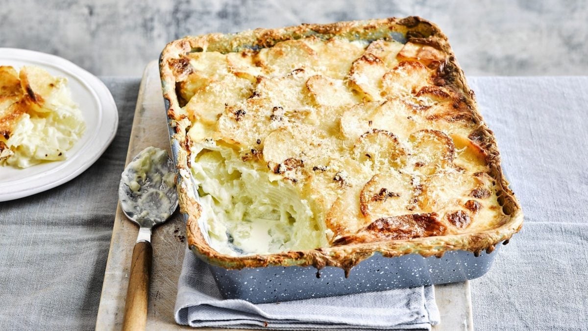 Gratin Dauphinois, mit dünn geschnittenen Kartoffelscheiben und einer dicken Schicht gratiniertem Käse, serviert in einer großen Auflaufform auf einem rustikalen Brett.