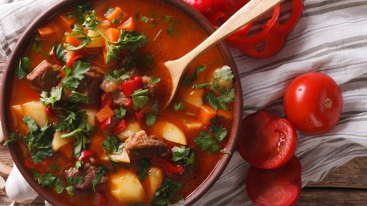Gulaschsuppe mit Fleisch, Kartoffeln und Gemüse in brauner Schüssel.