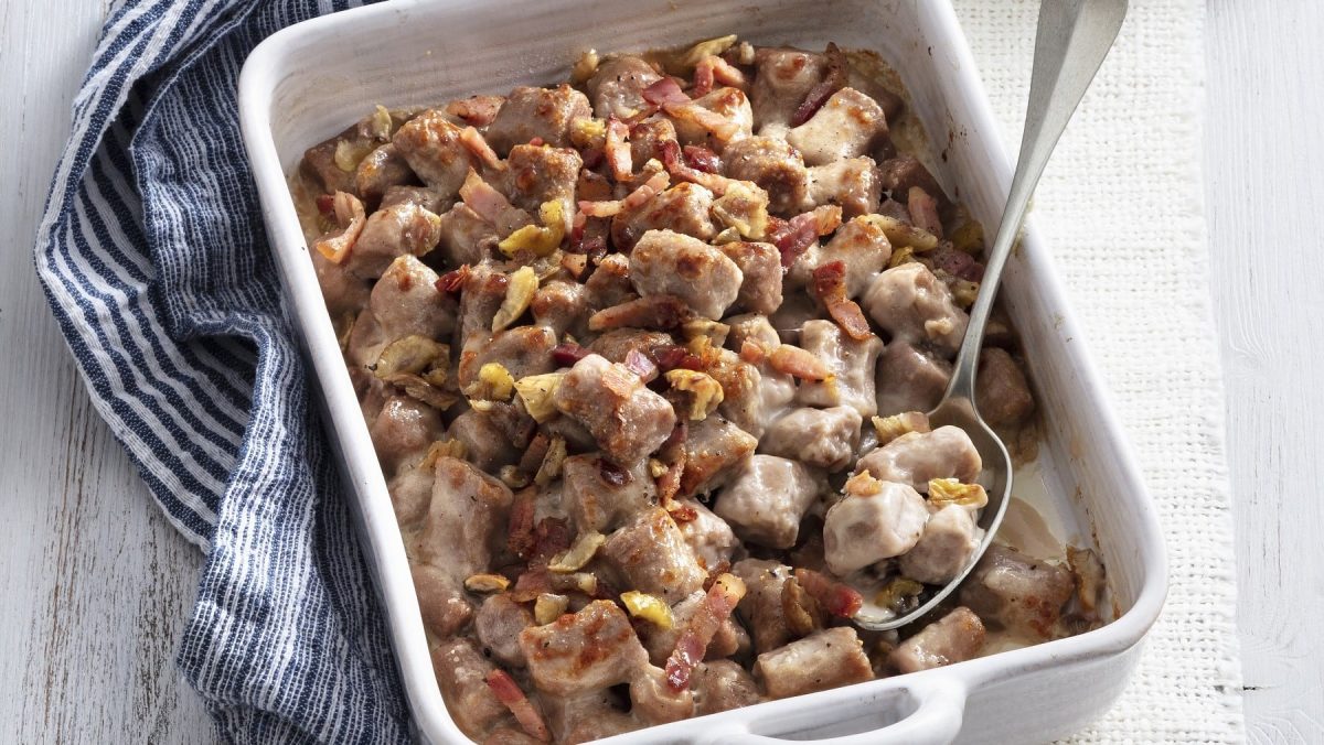 Maronen-Gnocchi mit Bacon, serviert aus der Auflaufform auf einem blauen Tischtuch.