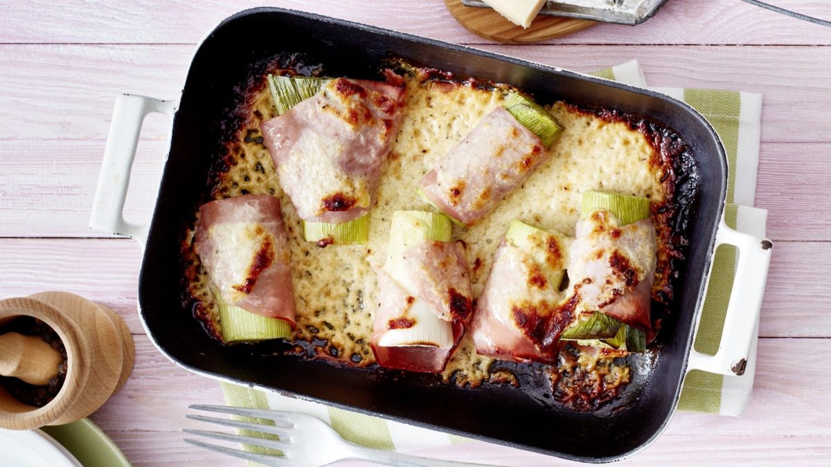 Ofen-Lauch überbacken mit Käse in einer schwarzen Ofenform vor hellem Hintergrund.